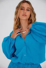 Conjunto de lino color celeste, compuesto por una camisa de manga larga abullonada con cuello camisero y dos bolsillos frontales, y un short con cintura elastizada y forro interno.