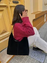 Bolso tipo tote de gamuza negra con cierre superior y asa de hombro.