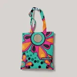 Bolso de tela tipo tote bag con estampado de flores de estilo retro en tonos turquesa, naranja, rosa y negro. Tiene asas de color turquesa.