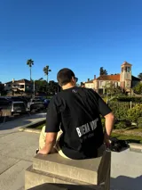 Remera negra de corte semi oversize con estampado en la espalda que dice "BIENA VIBRA feel the vibes" y un logo pequeño en el frente.