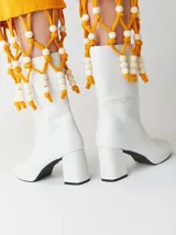 Botas de caña media de cuero sintético blanco con plataforma y tacón cuadrado. Presentan un detalle de cuentas de madera y cordón amarillo alrededor de la caña.