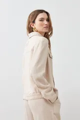 Chaqueta color beige melange de lino con pespuntes a contraste, cuello camisero, cierre frontal con botones, bolsillos de parche en el pecho y corte recto.