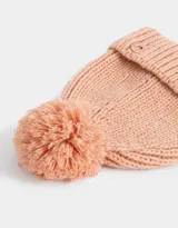 Gorro de lana tejido color rosa viejo, con pompón en la parte superior y etiqueta metálica con logo en el borde.