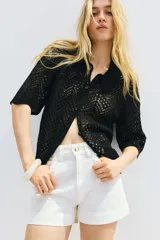 Camisa negra de manga corta en punto pointelle suave, con cuello y botones adelante. Ribete festoneado en mangas y bajo.