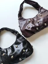 Cartera tipo baguette de cuero sintético, color negro, con apliques de tachas redondas plateadas.