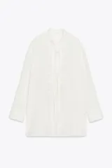 Camisa blanca a rayas verticales, de cuello redondo y manga larga con puños. Presenta cierre frontal con cordones ajustables con lazadas y abertura en la espalda ajustable con lazadas.