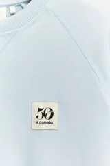 Sudadera celeste de algodón con cuello redondo y manga larga. Tiene un parche conmemorativo del 50 aniversario en el pecho y terminaciones en rib a tono.