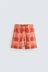 Short de baño color ladrillo con estampado de líneas curvas en color salmón. Tiene cintura elástica ajustable con cordón, bolsillos laterales y trasero.