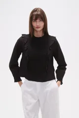 Blusa de algodón color negro con cuello a la base y detalle de volados en el frente. Posee mangas largas con puños elásticos y un panel frontal con textura fruncida.