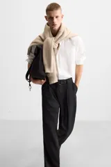 Pantalón negro de corte ancho con cinturón de tela con hebilla metálica y pliegues frontales.