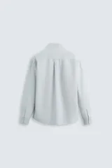 Camisa celeste a rayas verticales, de corte regular fit, confeccionada en tejido de algodón. Tiene cuello abotonado, manga larga con puños abotonados, bolsillo de parche en el pecho y cierre frontal con botones.