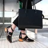 Zapato de cuero negro con detalle de charol, taco de madera con folia en cuero de 5cm, cierre YKK en talón, hebilla y elástico en el empeine.