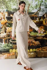 Blusa color blanco con cuello tipo polo, de manga larga y corte holgado. Presenta un bordado de cerezas en el pecho y cierre parcial con botones.