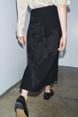 Falda larga negra de tiro medio confeccionada en hilatura con mezcla de algodón. Detalle de bordados florales a tono. Bajo evasé y cierre con cremallera oculta en costura.
