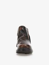 Bota corta de cuero bovino negro con efecto desgastado y envejecido, con detalles en gris claro. Presenta un diseño con solapa frontal que se ajusta con un broche y una cremallera lateral expuesta en el talón. Posee un taco bajo y cuadrado.