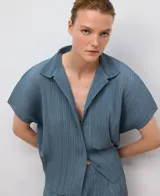 Camisa de poliéster reciclado color gris azul con textura crinkle. Presenta cuello solapa, manga corta redondeada y botonadura frontal oculta.