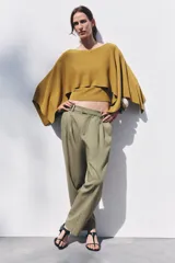 Pantalón color verde oliva de tiro medio con cintura con trabillas, bolsillos laterales, pinzas delanteras y raya planchada. Cierre frontal con cremallera, botón y ganchos metálicos.