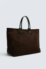 Bolso tipo shopper marrón oscuro, fabricado en cuero con acabado serraje. Tiene un compartimento principal con cierre magnético y un bolsillo interior con cremallera. Cuenta con dos asas de mano de cuero.