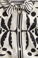 Camisa de corte holgado con estampado floral en blanco y negro, cuello clásico, mangas largas y cierre frontal con botones.