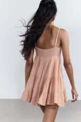 Vestido corto color salmón, de escote recto y tirantes finos ajustables. Presenta detalle de encaje en el escote y falda de tres niveles.