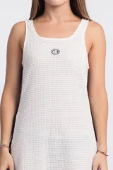 Vestido corto de punto waffle color crudo, con cuello redondo y sisas con ribete marrón. Presenta un logo bordado en el pecho y una banda lateral marrón.