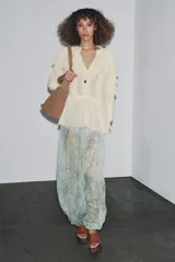 Blusa color crudo confeccionada en viscosa, con cuello redondo, escote en pico, mangas largas con puños elásticos, volantes frontales y detalles de encaje.