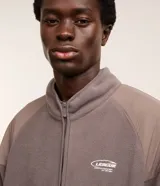 Saco masculino confeccionado en fleece color gris con recortes en marrón y negro, cuello alto, cierre en cremallera, cintura y puños ajustados con elástico. La prenda posee estampa localizada en el pecho con la palabra "LEAGUE".