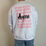 Buzo blanco de cuello redondo y corte oversize, con estampado en la espalda de la palabra "Amore" en rosa y negro.