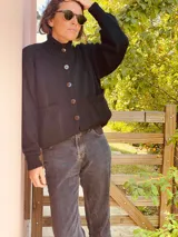 Cardigan negro de lana con cuello alto, cierre frontal con botones grandes, mangas largas y bolsillos delanteros.