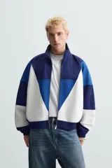Chaqueta deportiva azul marino, azul y blanca con cuello alto, cierre frontal con cremallera, bolsillos laterales y puños y bajo acanalados.