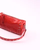 Bandolera marrón de cuero con tachas plateadas y correa de cuero con tachas plateadas. Tiene dos asas desmontables, una corta con tachas para llevarla en la mano o al hombro y una larga para llevarla al hombro o cruzada.