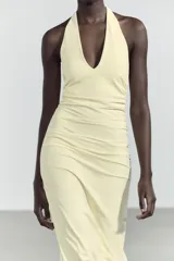 Vestido largo color amarillo pálido, con cuello halter que se ata en la nuca, escote en pico y frunces laterales.