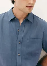 Camisa celeste de manga corta con cuello clásico, cierre frontal con botones y bolsillo de parche en el pecho. Corte recto.