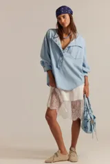 Camisa de denim chambray celeste, estilo oversized, con escote henley alargado con botones, hombros caídos y mangas abullonadas con puños terminados en volados.