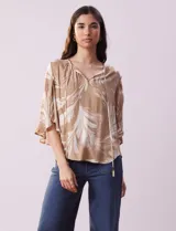 Blusa de crepe color beige con estampado de hojas blancas, cuello redondo con escote en V y lazo de ajuste, mangas 3/4 con tajo.