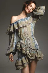 Vestido corto con estampado paisley en tonos ocre, azul y marrón. Tiene escote recto con volantes, mangas largas abullonadas con puños elásticos y cintura elástica.