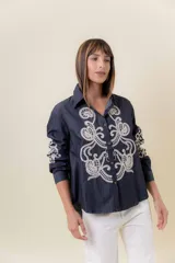 Camisa de denim liviano color azul oscuro con bordado artesanal en tono crudo en el frente y en las mangas. Presenta cuello clásico y cierre frontal con botones, con un calce relajado.
