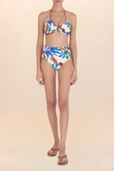 Calzón de bikini tiro alto con frunces laterales y estampado botánico en tonos azules, marrones y verdes sobre fondo blanco.