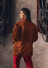 Campera marrón de gamuza con corte masculino, hombros marcados y caída recta. Presenta flecos largos en la espalda y mangas.