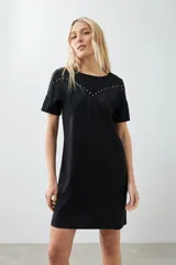 Vestido corto negro con flecos en el pecho y tachas plateadas en los hombros.