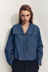 Camisa celeste de algodón con efecto denim, cuello bobo, escote pico, manga larga con puños y cierre frontal con botones.