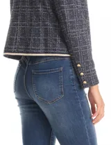 Chaqueta de tweed azul con sutiles destellos de lúrex, cuello a la base y abertura frontal. Tiene bolsillos delanteros decorativos y manga larga con tres botones metálicos dorados en cada puño. Las terminaciones del cuello, apertura frontal, bolsillos y ruedo tienen vivos a contratono. Forro interno a tono.