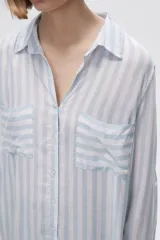 Camisa a rayas verticales grises y blancas, con cuello camisero, cierre frontal con botones, mangas largas con trabillas para enrollar y dos bolsillos de parche en el pecho.