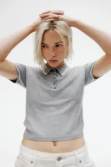 Remera polo corta de punto fino color gris con cuello, tapeta de botones y mangas cortas con ribete blanco.