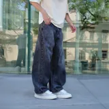 Pantalón de jean negro con lavado oscuro y efecto desgastado, de corte ultra ancho y tiro alto. Presenta un parche circular con logo en el bolsillo trasero derecho.