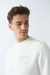 Buzo de felpa color crudo, de corte recto, con cuello redondo, puños y ruedo acanalados.