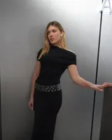 Vestido largo negro de corte ajustado, con escote asimétrico y cinturón con apliques metálicos.