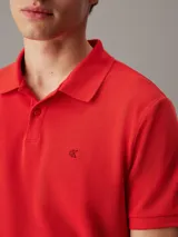Chomba roja de piqué de algodón, corte regular, cuello clásico, cartera de botones, bajo con aberturas laterales y logo de Calvin Klein bordado en el pecho.