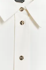 Camisa blanca de satén con cuello solapa y manga larga. Cierre frontal con botones dorados.