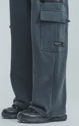Pantalón de jogging gris oscuro, de corte amplio, con cintura y puños elásticos, bolsillos laterales y trasero, y bolsillo lateral adicional con cierre.